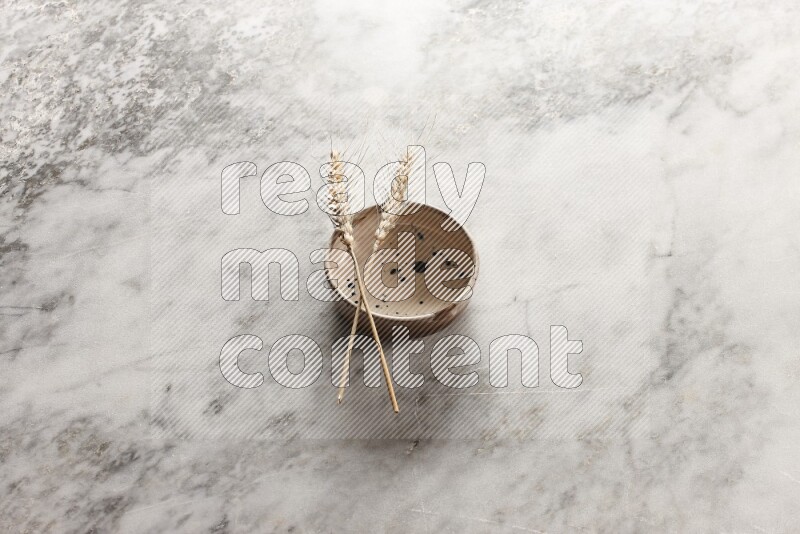 Wheat stalks on multicolored pottery bowl on grey marble background
