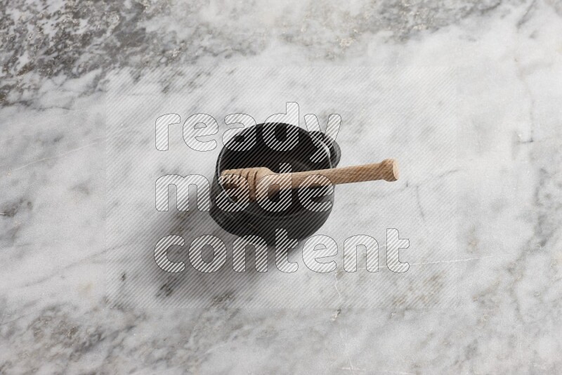 Black pottery bowl with wooden honey dipper in it on grey marble background