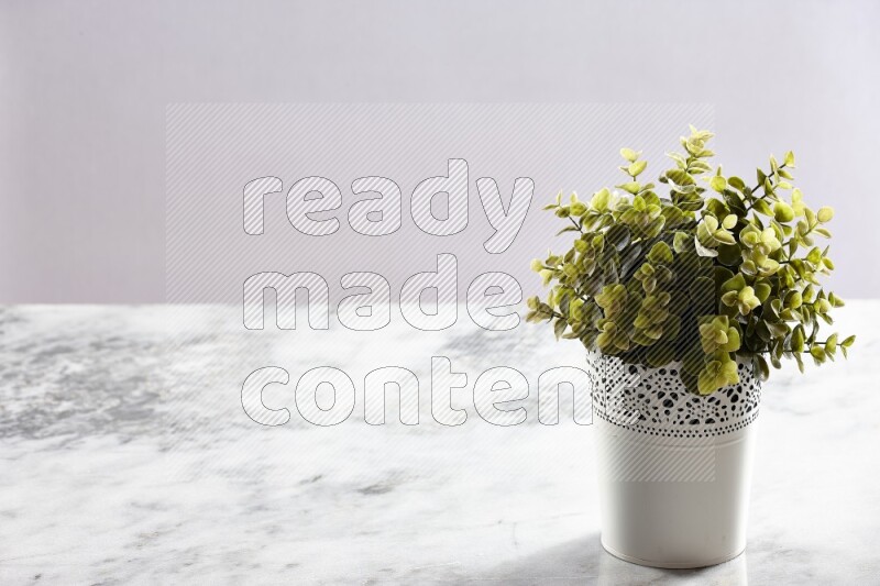 Green artificial plant in white decorative pot on grey marble background