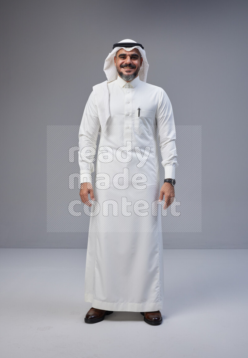 Saudi man Wearing Thob and white Shomag standing interacting with the camera on Gray background