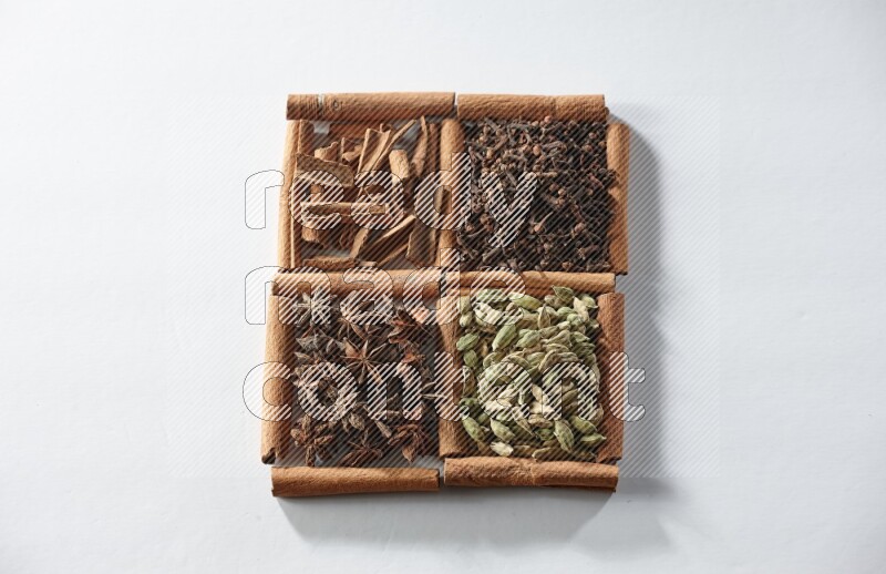 4 مربعات من أعواد القرفة ممتلئة بالهيل واليانسون النجمي والقرنفل والقرفة على أرضية بيضاء