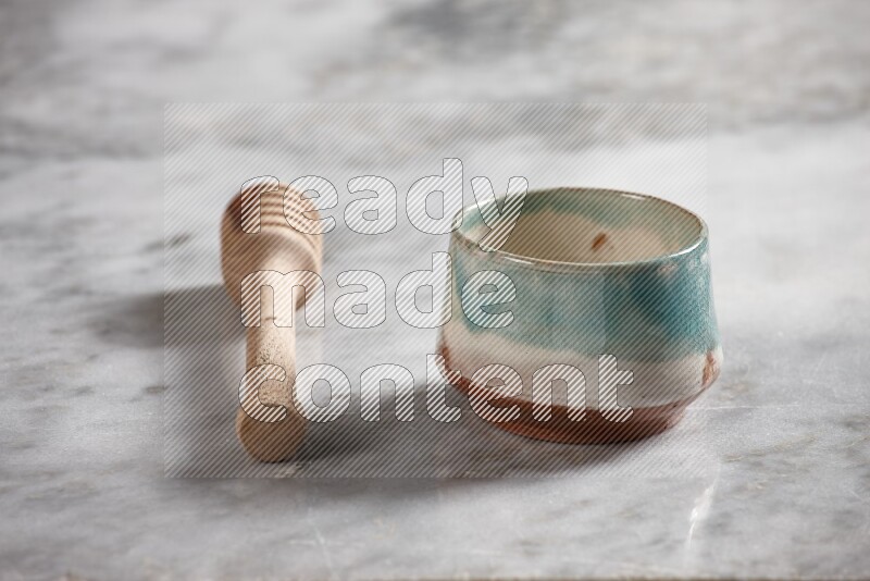 Multicolored pottery bowl with wooden honey dipper on the side on grey marble background