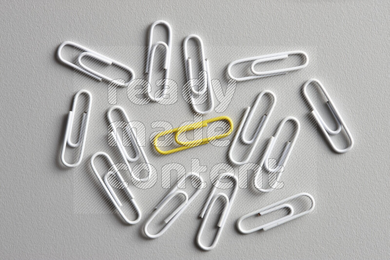A bunch of white paper clips with a different colored paper clip in the center on grey background