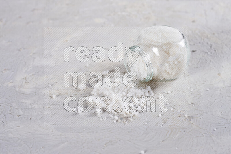 A glass jar full of coarse sea salt crystals on white background