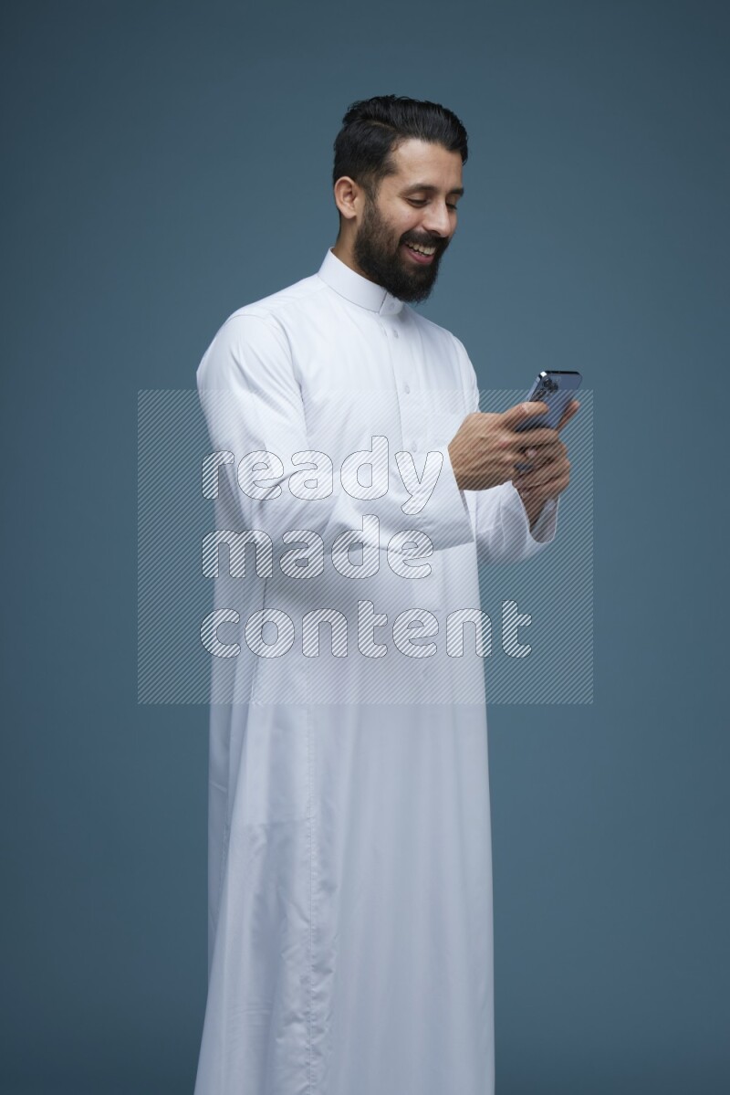 A man Texting in a blue background wearing Saudi Thob