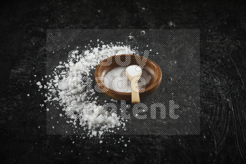 A pottery plate full of fine salt with bunch of coarse salt beside it on black background