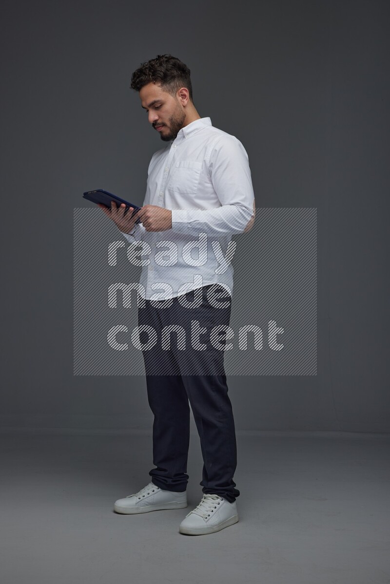 A man wearing smart casual standing and using his tablet eye level on a gray background