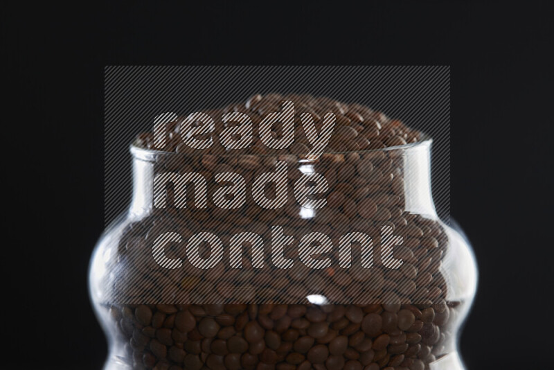 Brown lentils in a glass jar on black background