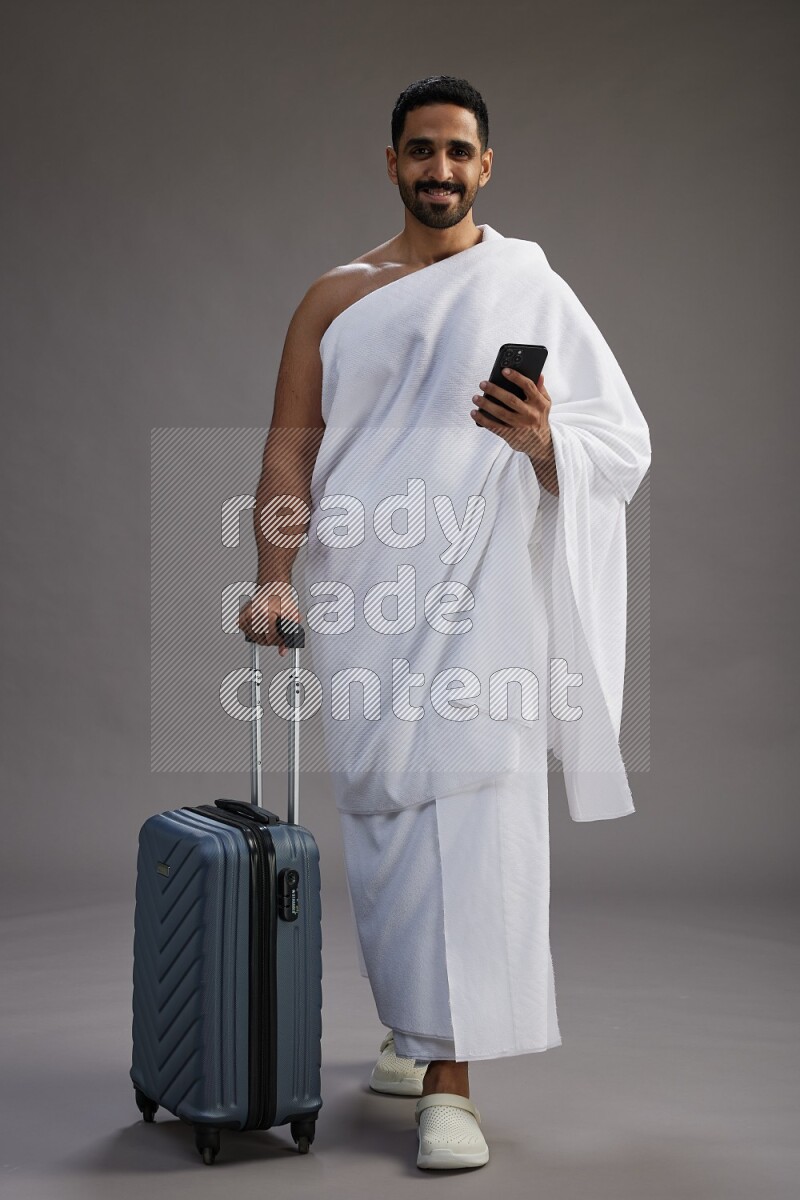 A man wearing Ehram Standing holding traveling bag on gray background