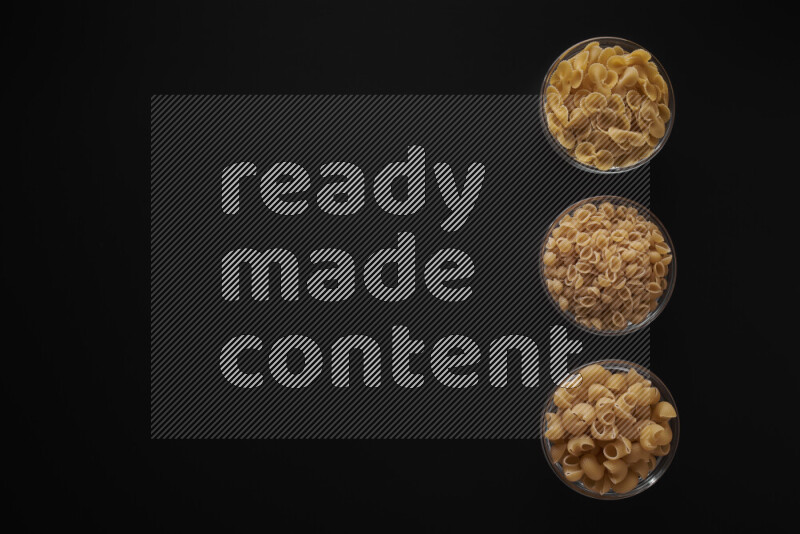 Different pasta types in 3 glass bowls on black background