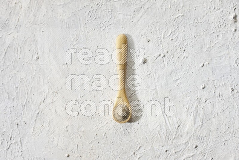 A wooden spoon full of white pepper powder on textured white flooring