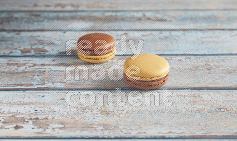 45º Shot of two Yellow and Brown Chai Latte macarons on light blue wooden background