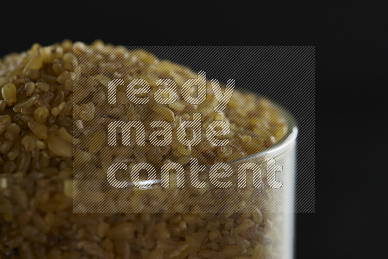 Coarse bulgur in a glass jar on black background
