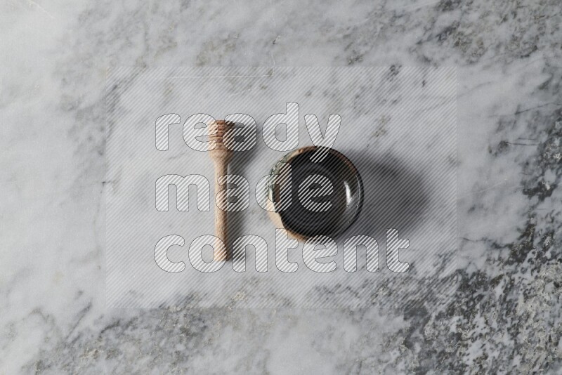 Multicolored pottery bowl with wooden honey dipper on the side on grey marble background