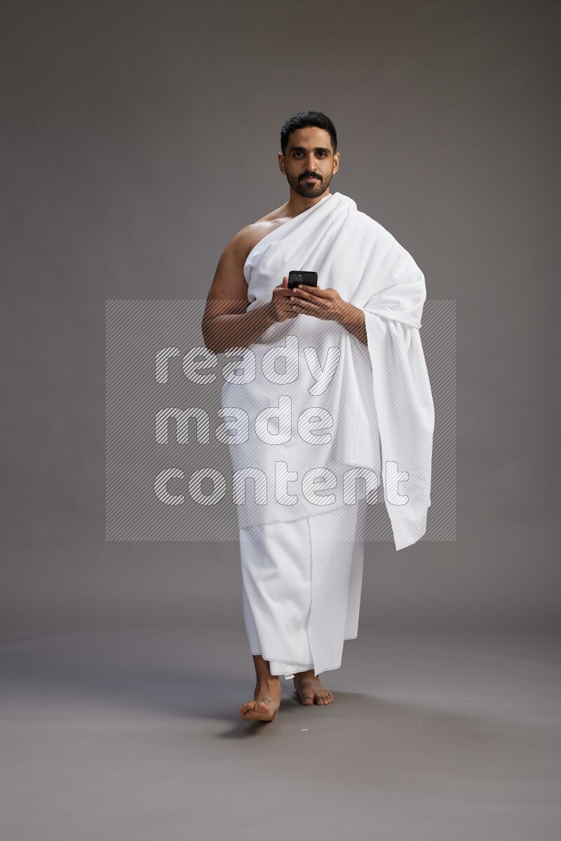 A man wearing Ehram Standing texting on phone on gray background