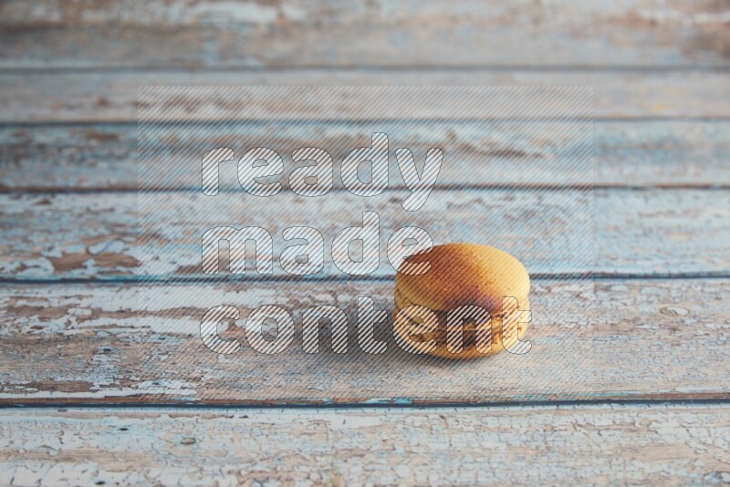45º Shot of Yellow Crème Brulée macaron on light blue wooden background