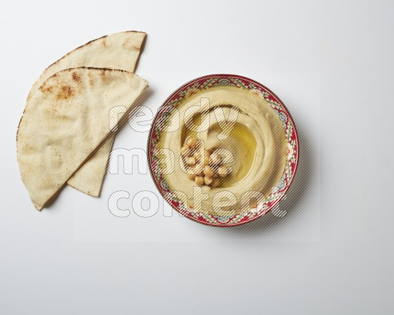 Hummus in a red plate with patterns garnished with roasted chickpeas  on a white background