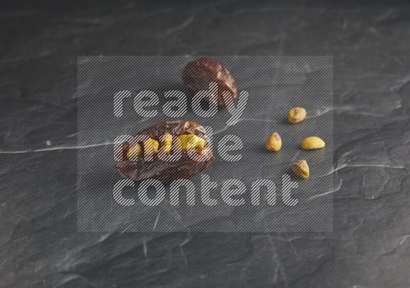 two pistachios stuffed madjoul dates on a black textured background