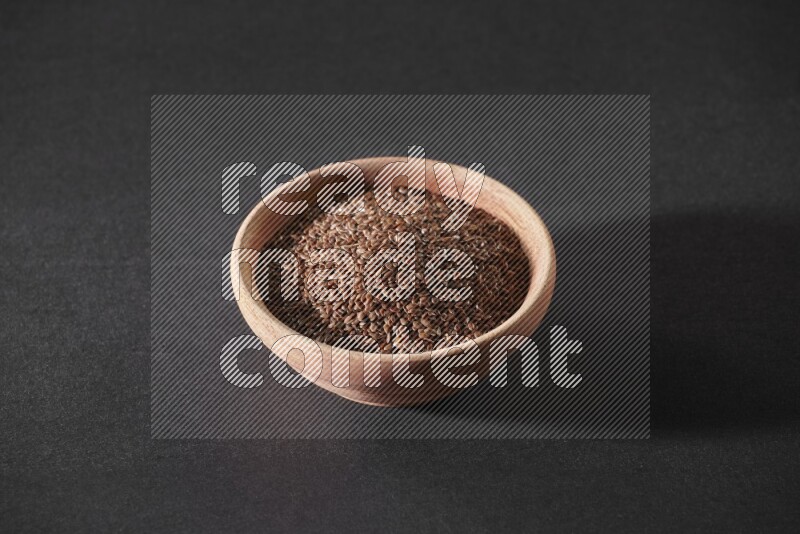 A wooden bowl full of flaxseeds on a black flooring