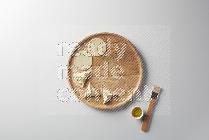 two closed sambosas and one open sambosa filled with cheese while oil with oil brush aside in a wooden dish on a white background