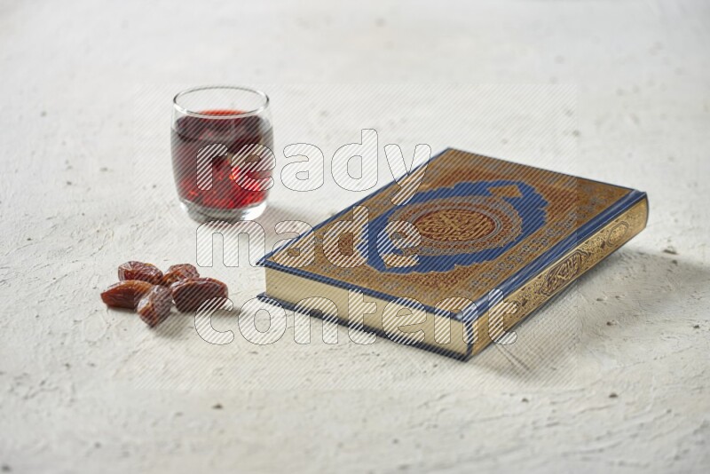 Quran with dates, prayer beads and different drinks all placed on textured white background