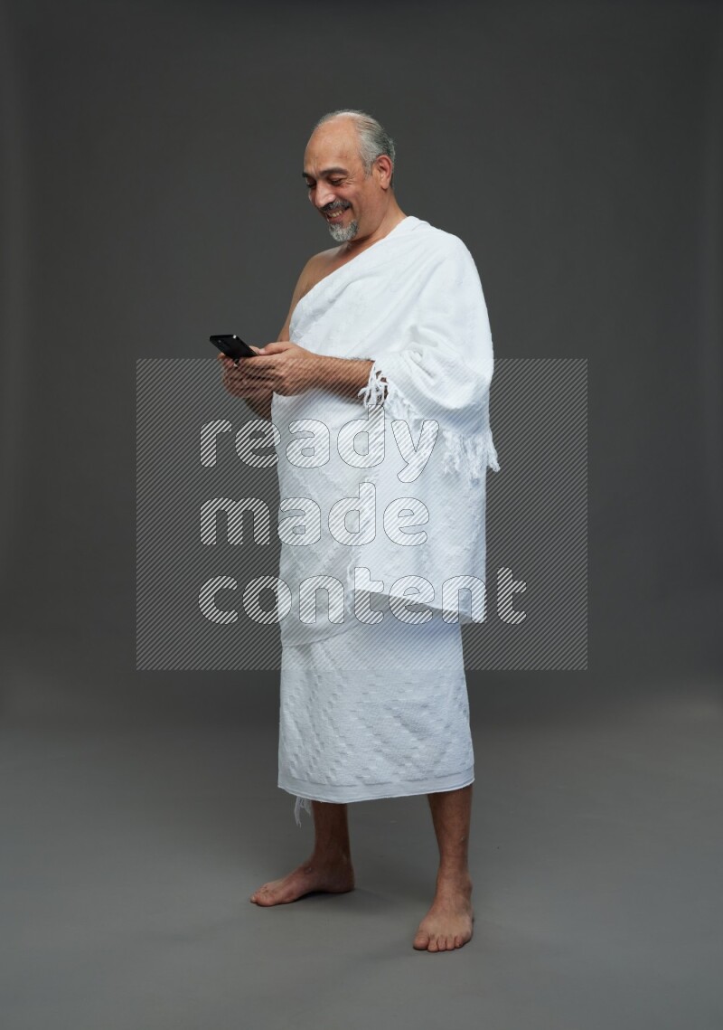 A man wearing Ehram Standing texting on phone on gray background