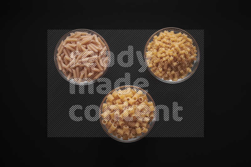 Different pasta types in glass bowls on black background