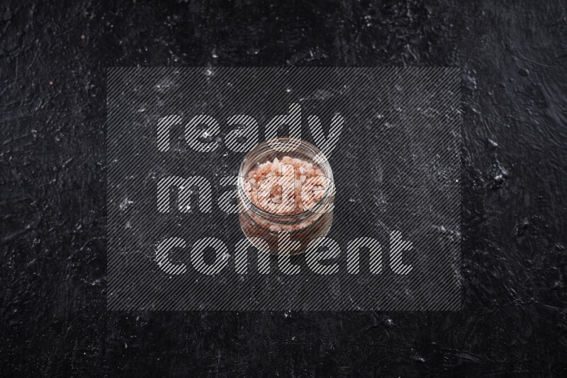 A glass jar full of coarse himalayan salt crystals on black background
