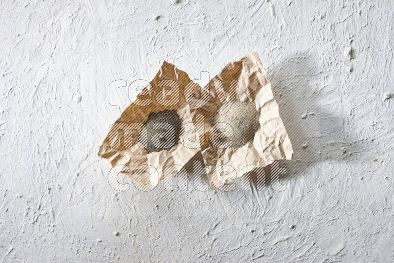 2 Crumpled pieces of paper full of black and white pepper powder on a textured white flooring