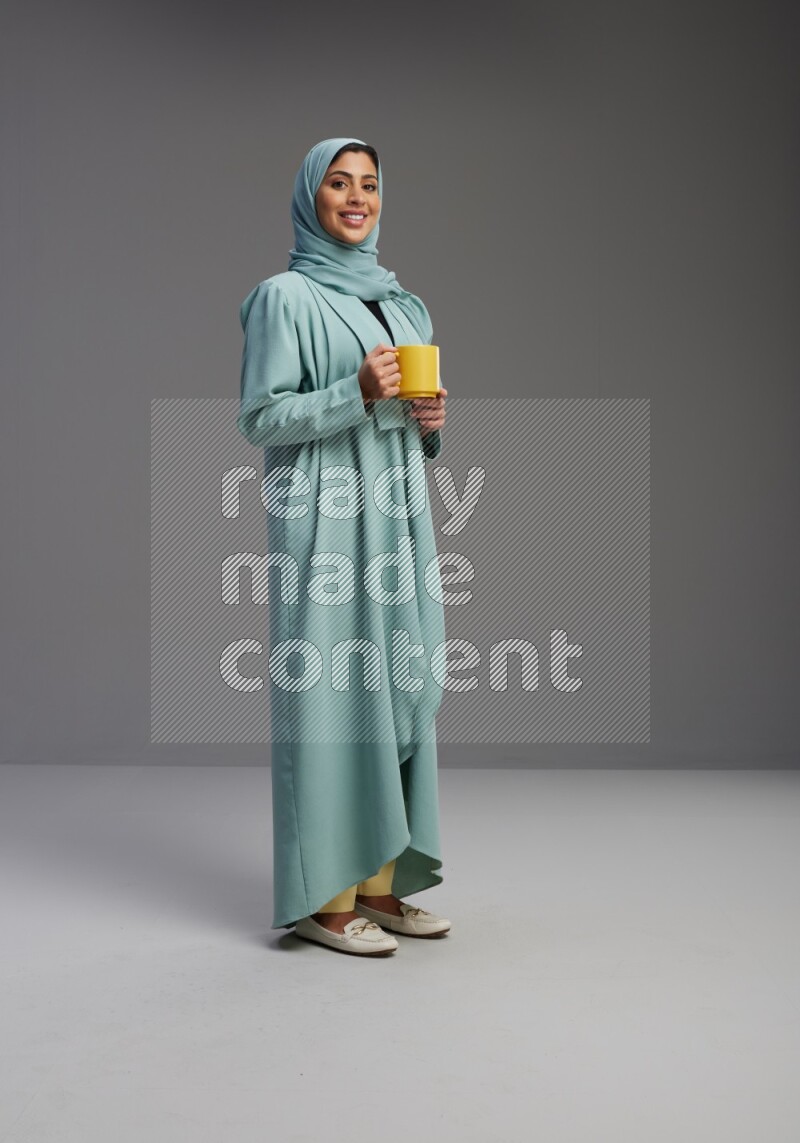 Saudi Woman wearing Abaya standing  holding a mug on Gray background