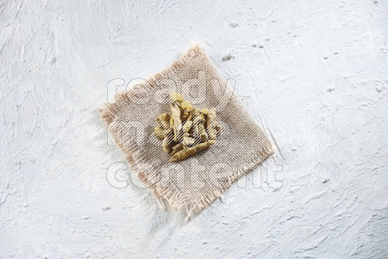 Dried turmeric whole fingers on a piece of burlap on a textured while flooring