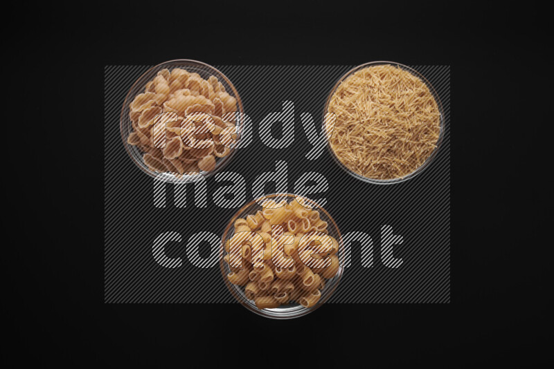 Different pasta types in glass bowls on black background