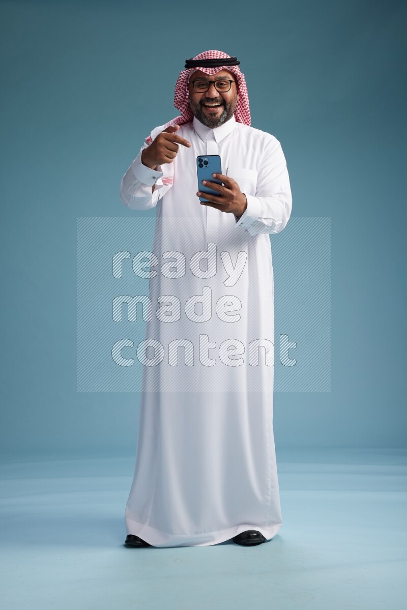 Saudi Man with shimag Standing texting on phone on blue background