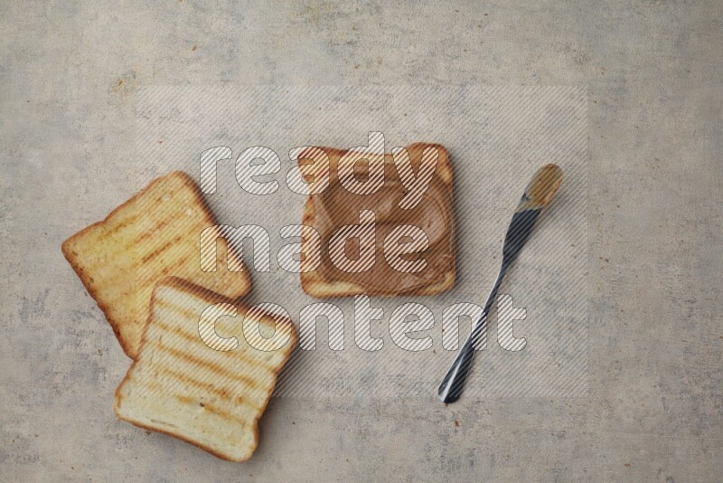 Creamy peanut butter on a toasted white toast and toasted white toast slices on a light blue textured background