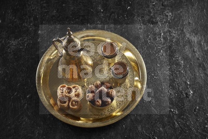 Oriental sweets with dates and a drink on a metal tray in a dark setup