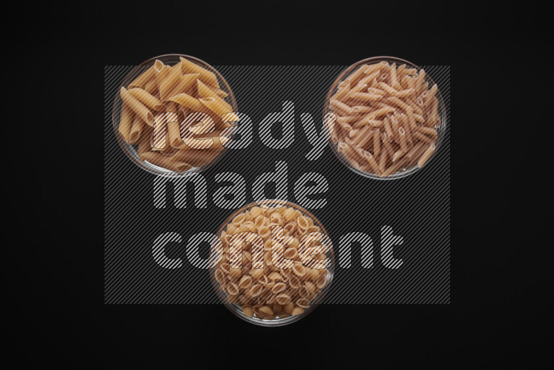 Different pasta types in glass bowls on black background