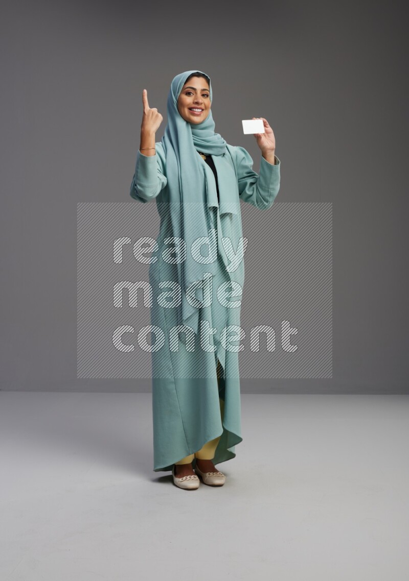 Saudi Woman wearing Abaya standing holding ATM card on Gray background