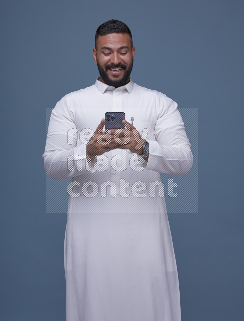 A man Texting on Blue Background wearing Saudi Thob