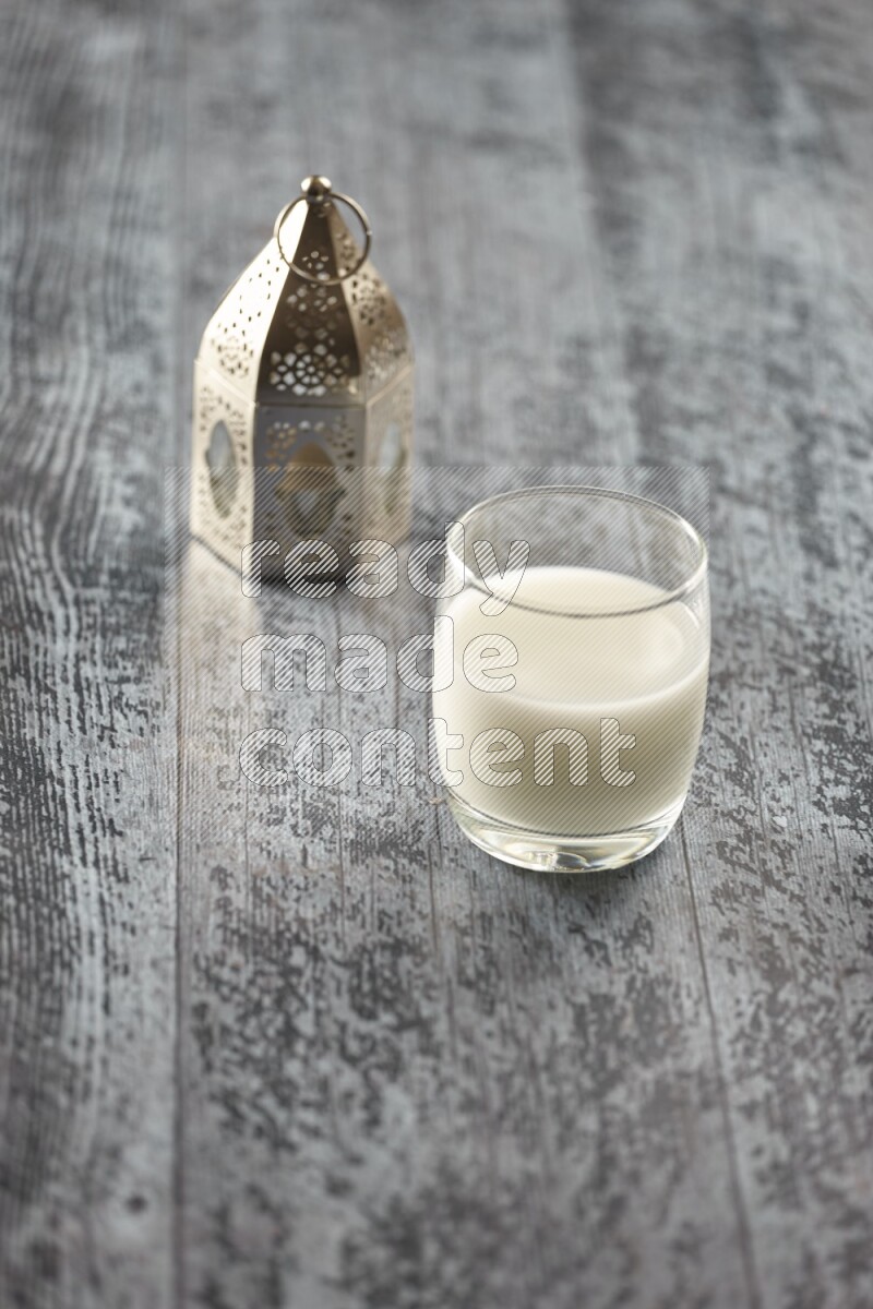 A silver lantern with different drinks, dates, nuts, prayer beads and quran on grey wooden background