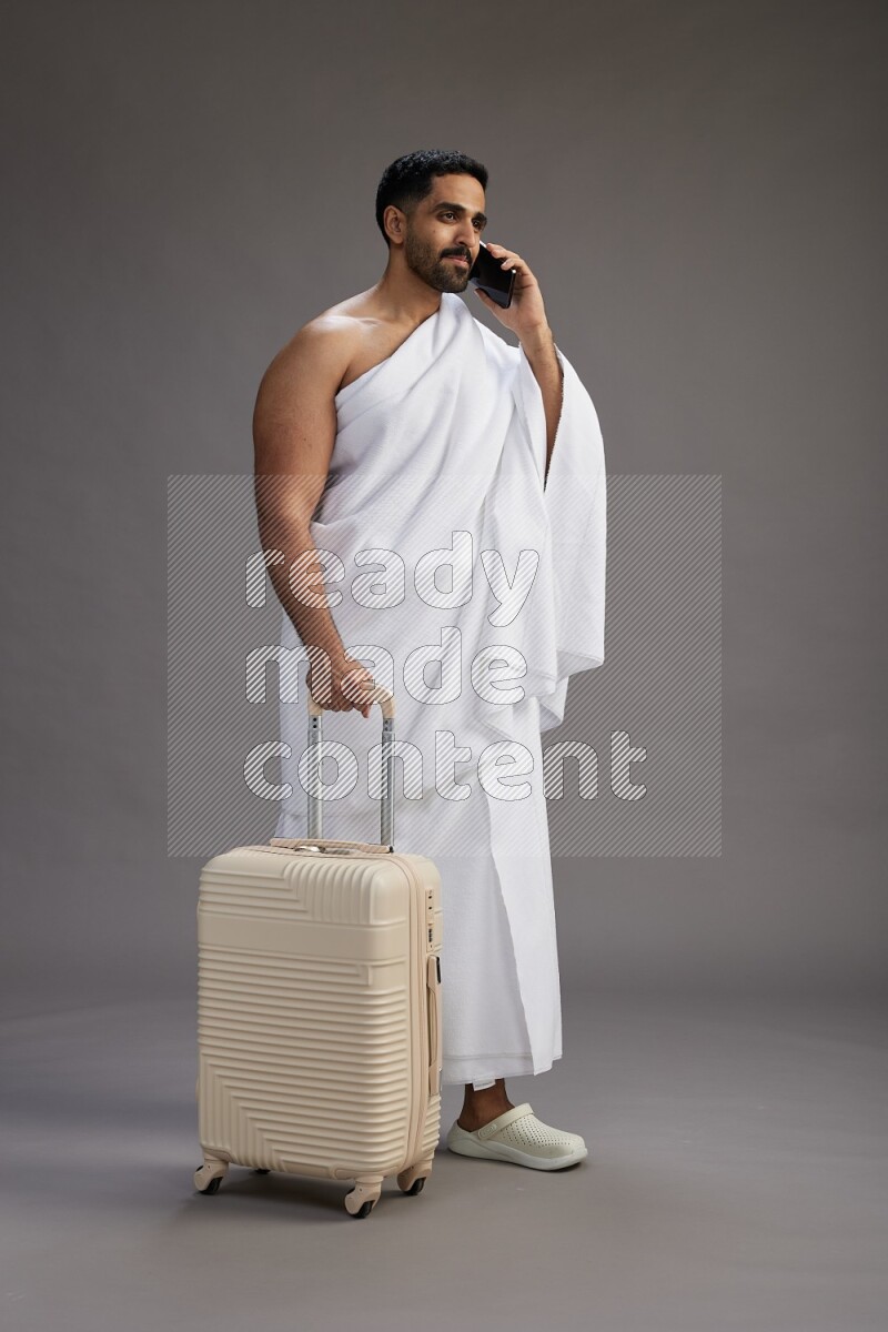 A man wearing Ehram Standing holding traveling bag on gray background