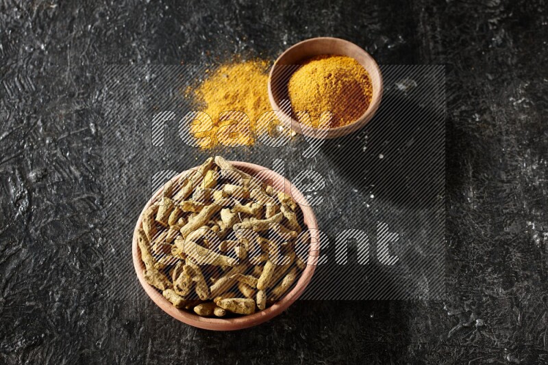 وعاءان خشبيان، أحدهما ممتلئ ببودرة الكركم والآخر بأصابع الكركم المجففة، على خلفية سوداء