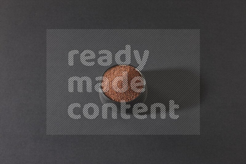 A black pottery bowl full of garden cress seeds on a black flooring