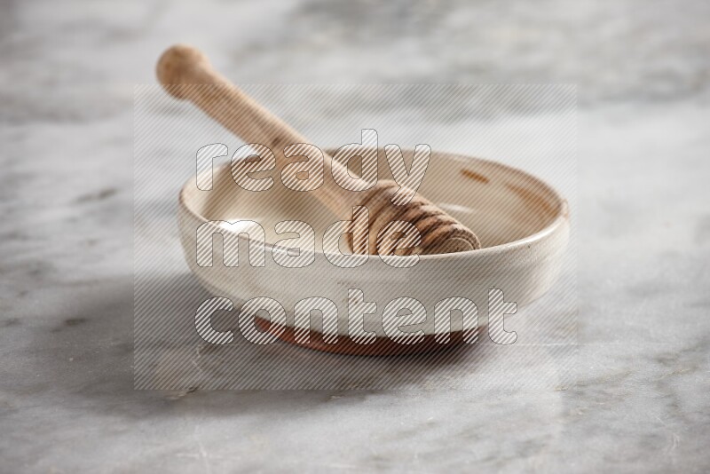 Beige pottery bowl with wooden honey dipper in it on grey marble background
