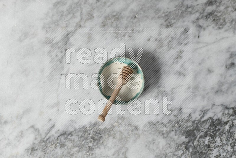 Multicolored pottery bowl with wooden honey dipper in it on grey marble background