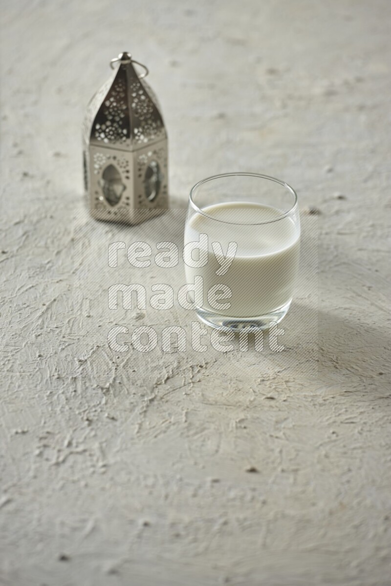 A silver lantern with different drinks, dates, nuts, prayer beads and quran on textured white background