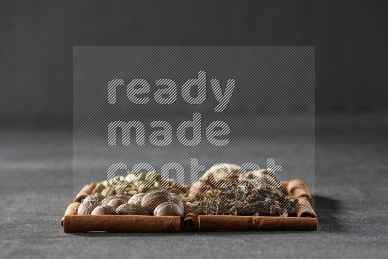 4 squares of cinnamon sticks full of dried basil, cardamom, dried ginger and nutmegs on black flooring