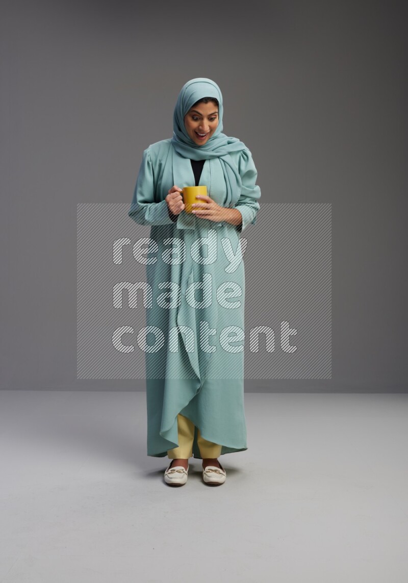 Saudi Woman wearing Abaya standing  holding a mug on Gray background