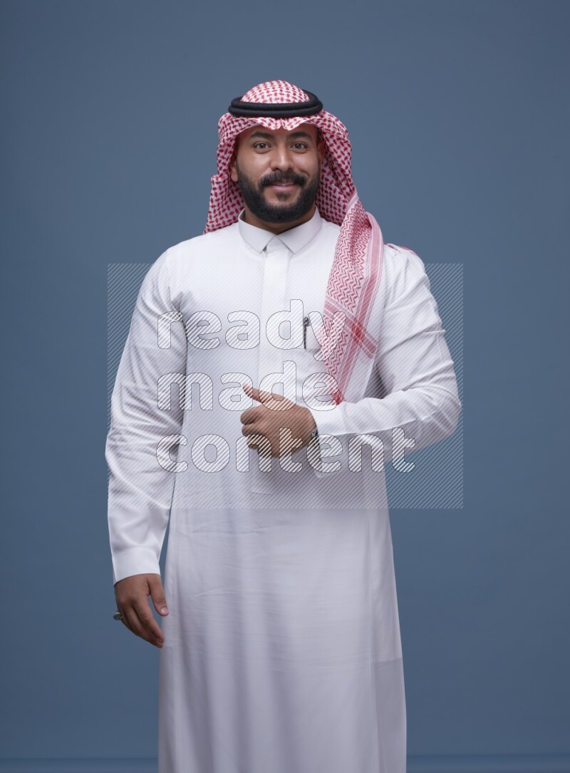 A Saudi man posing on blue background wearing Thob and Shomag