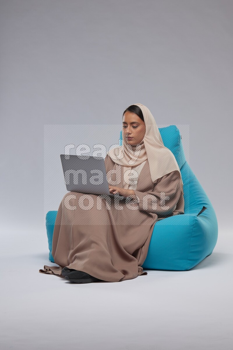 A Saudi woman sitting on a blue beanbag and working on laptop