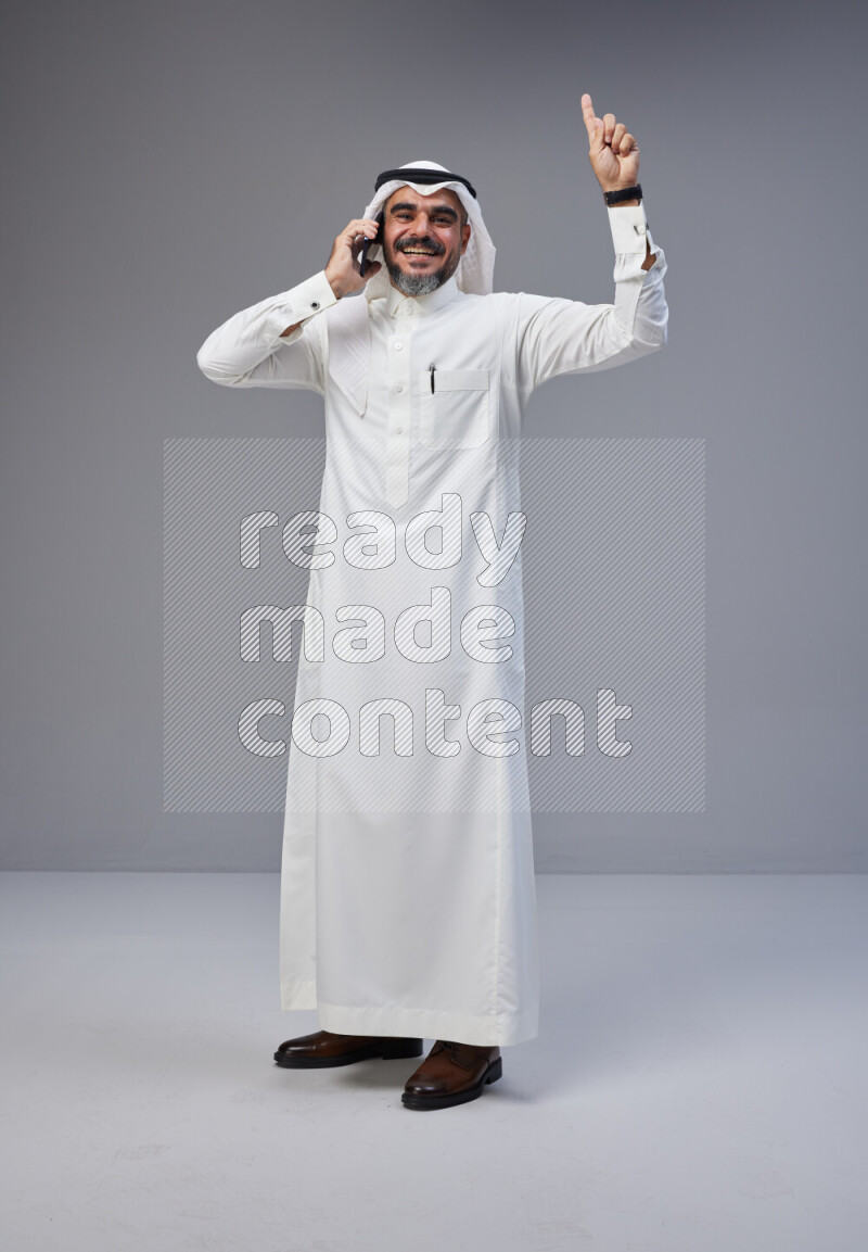 Saudi man Wearing Thob and white Shomag standing talking on phone on Gray background